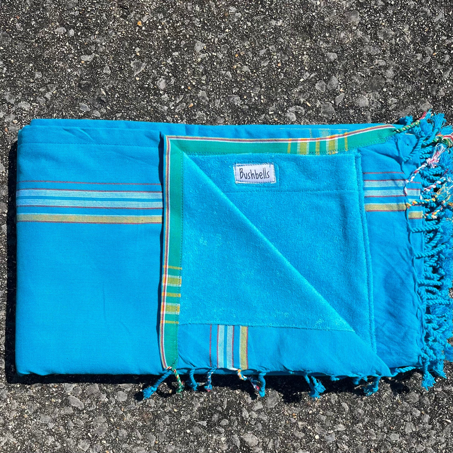 Blue kikoy towel with green stripes and fringes on a textured surface
