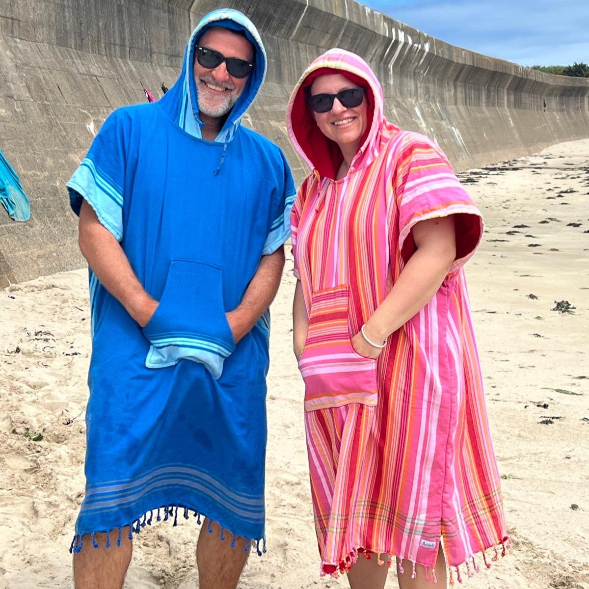 Two people wearing colorful hooded towels on a beach.